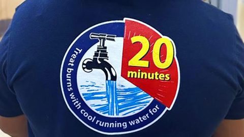 Nurse faces away from camera showing graphic on back of their shirt reading "Treat burns with cool running water for 20 minutes."