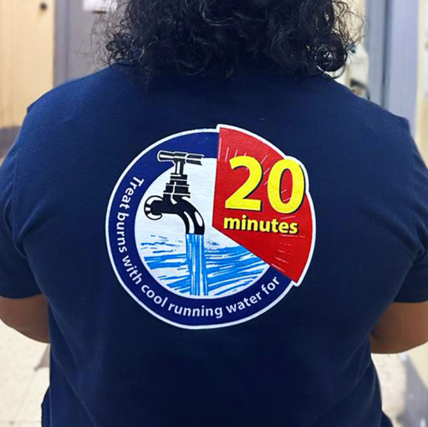 Nurse faces away from camera showing graphic on back of their shirt reading "Treat burns with cool running water for 20 minutes."