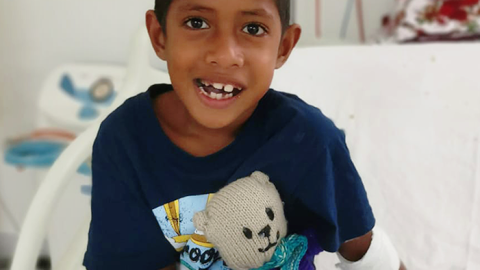 Joseph, a young boy, sitting up in his hospital bed, smiling at the camera.
