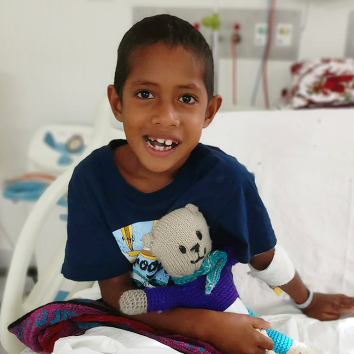 Joseph, a young boy, sitting up in his hospital bed, smiling at the camera.