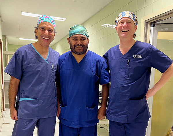 Three surgeons standing in a line, smiling joyfully.