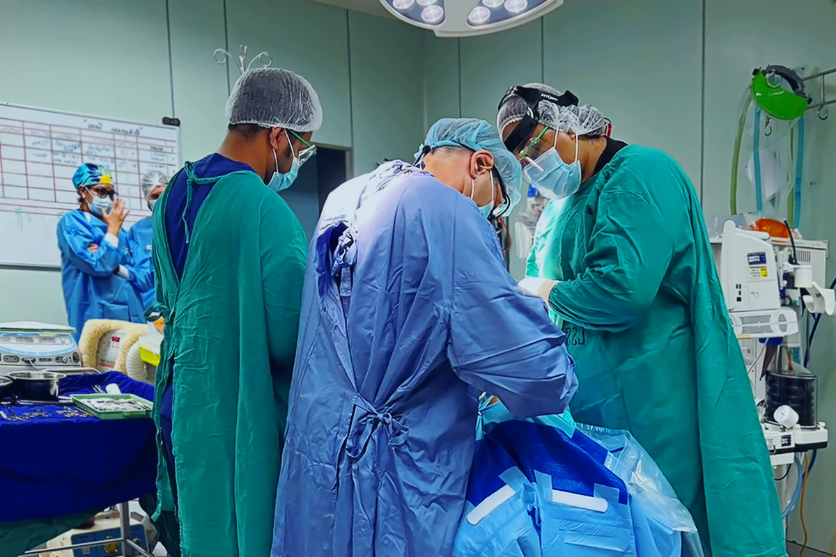 A team of people in personal protective equipment perform surgery on an unseen patient.