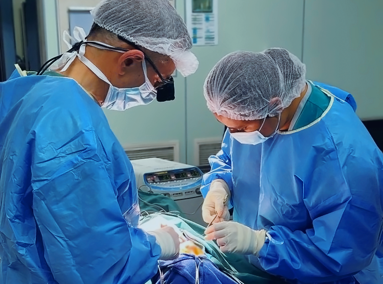 Two surgeons in full surgical scrubs focus intently on the procedure they are performing.
