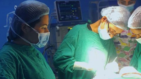 A group of four people in surgical scrubs perform surgery under a bright, direct light.