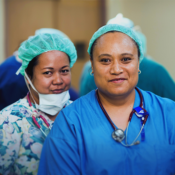 Two women wearing hospital scrubs smile at the camera.