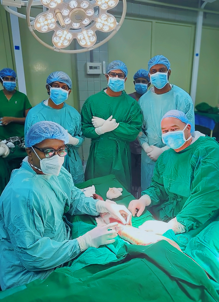 Surgical team of seven look up at the camera during a procedure on an unseen patient’s arm. 