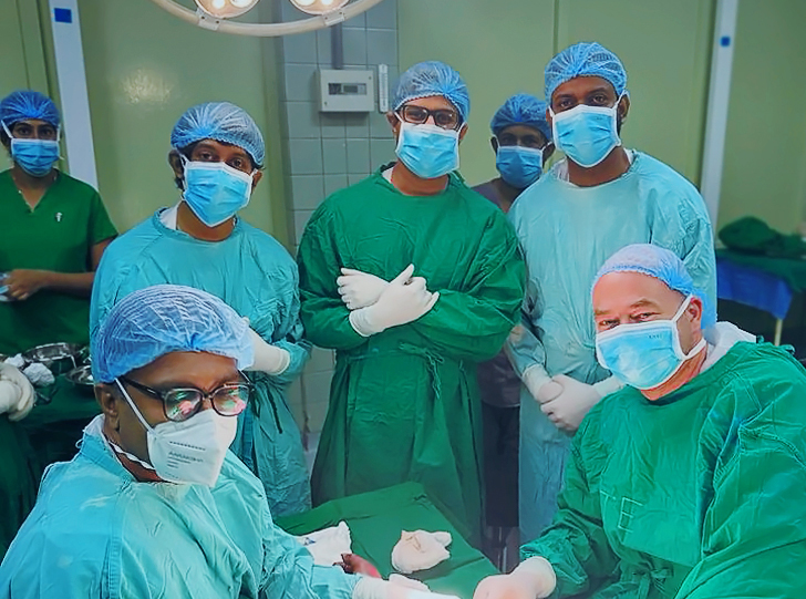 Surgical team of seven look up at the camera during a procedure on an unseen patient’s arm.