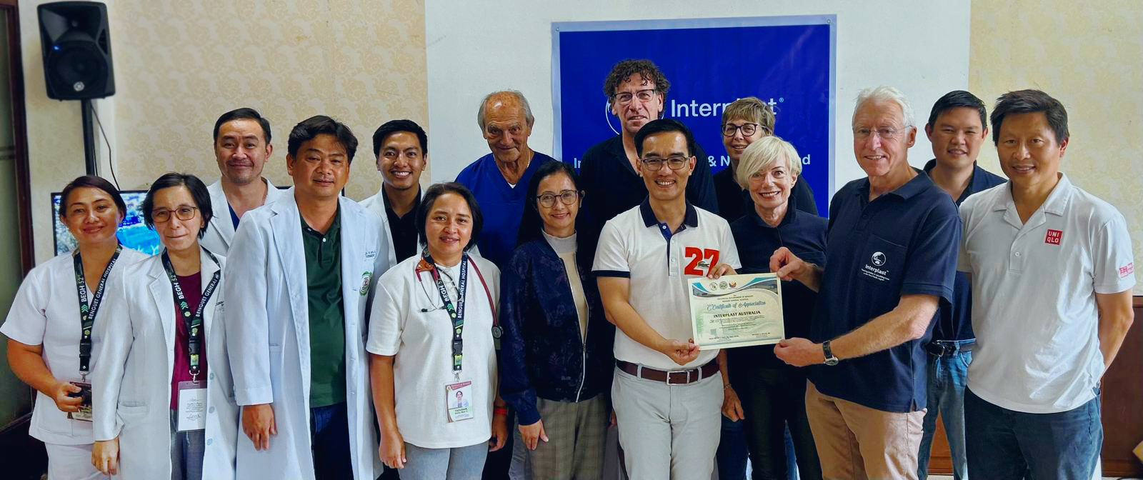 A group of people stand in front of a banner with Interplast’s logo and smile for the camera. Two hold a certificate.
