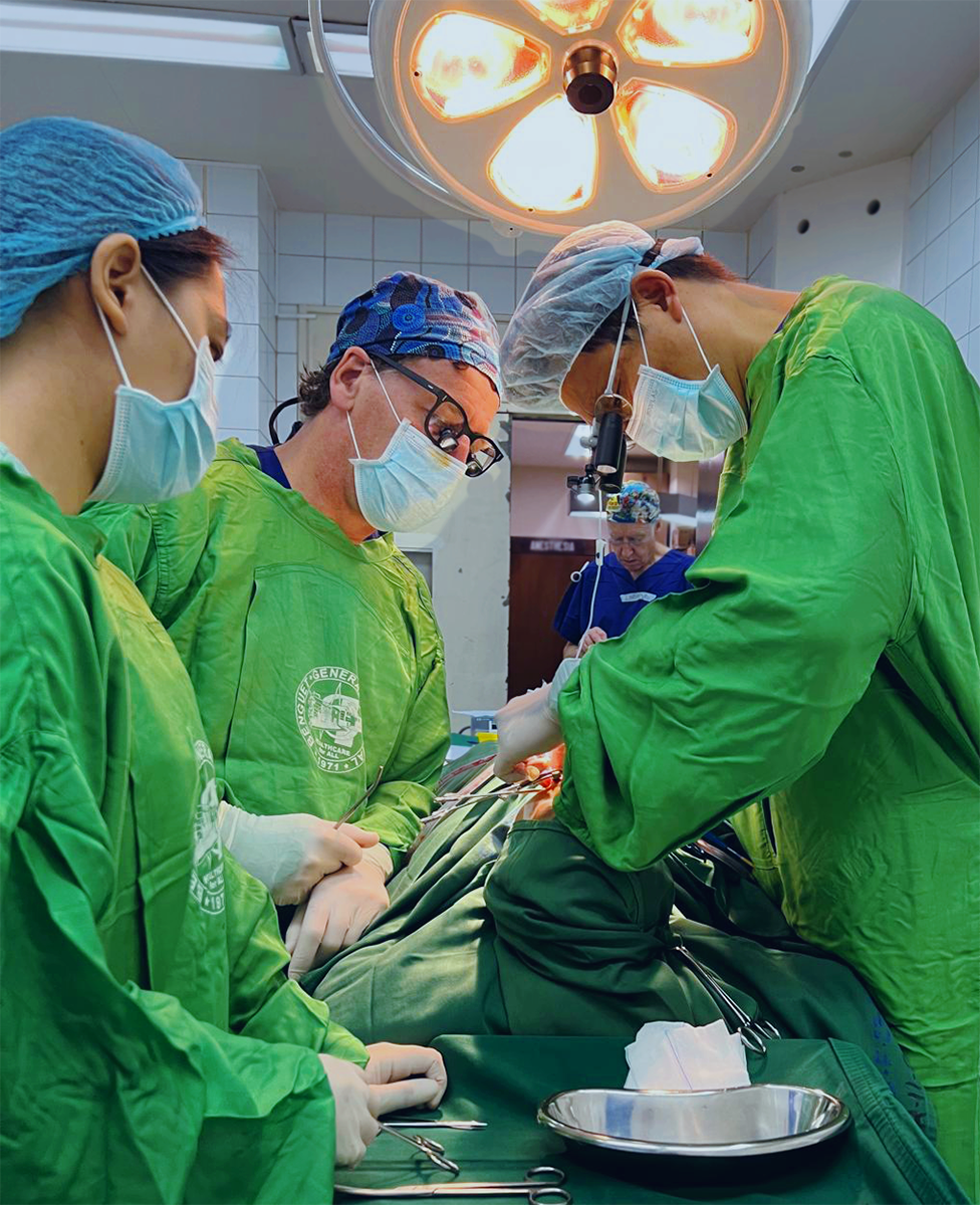 A team of three people dressed in surgical scrubs operate on the face of an unseen patient.