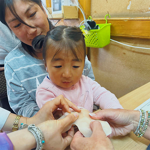 A young child has her hand measured for a hand splint while sitting in her mother’s lap.