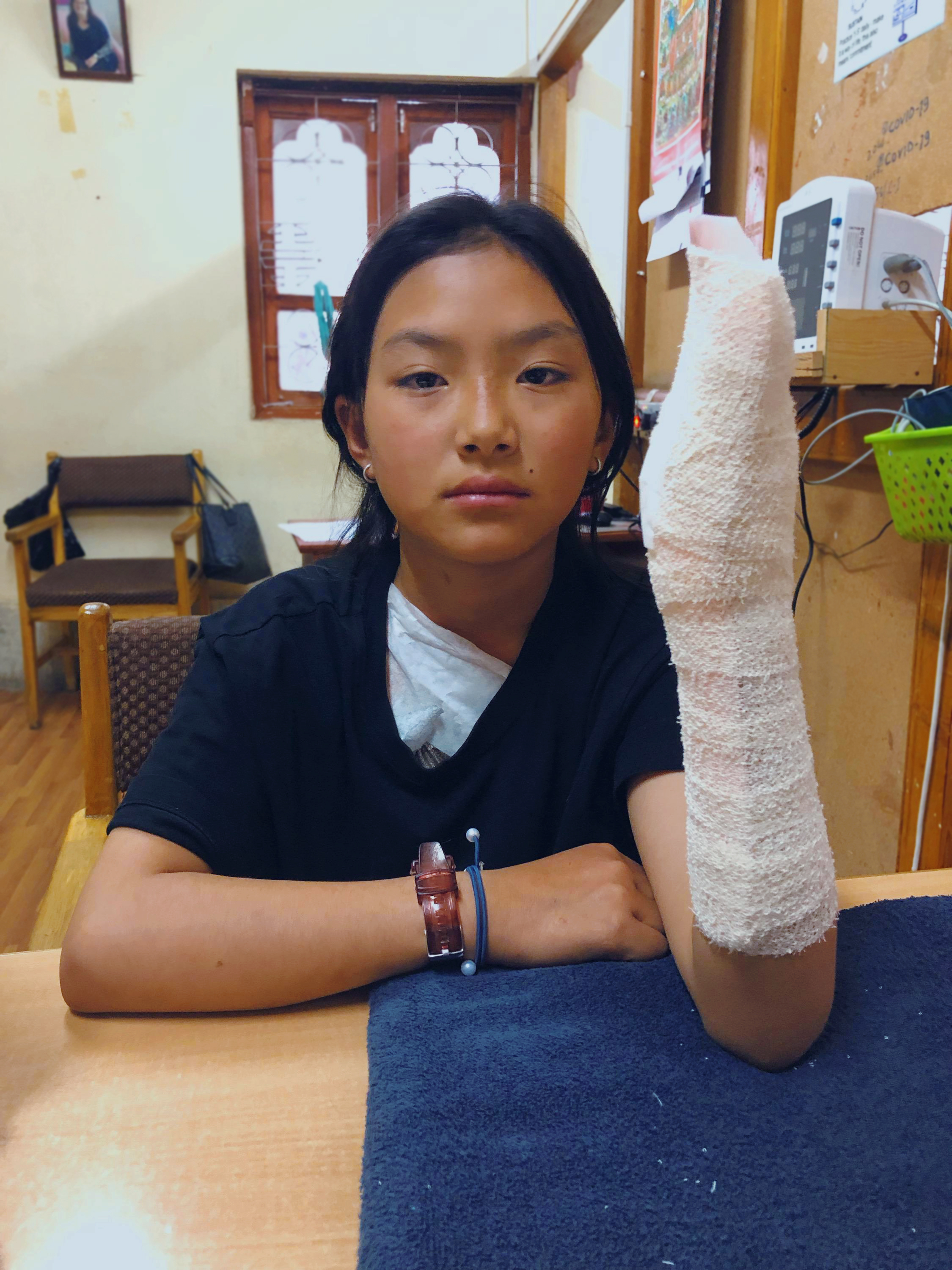 A young girl sits with her left hand bandaged and supported with a splint.