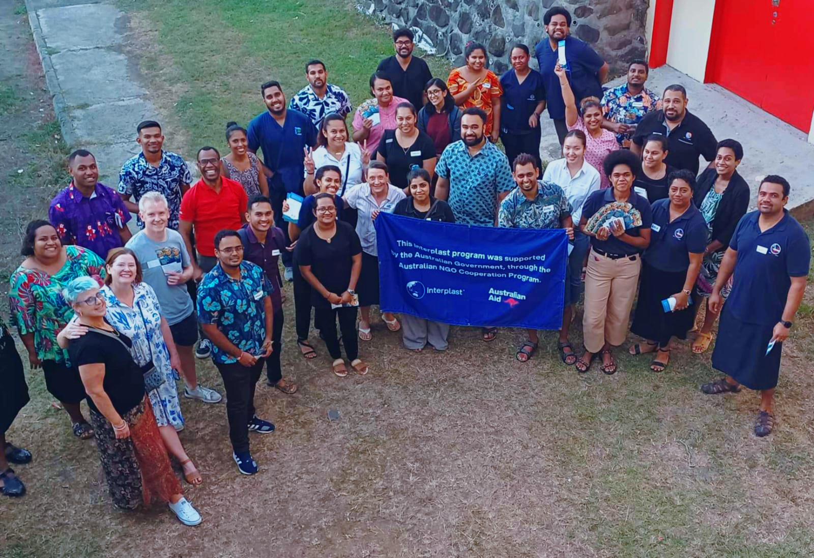 A large group of people, smile up at the camera. Some hold a banner showing the Interplast and Australian Aid logos.