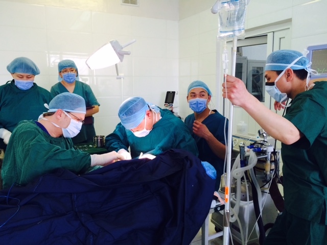 A group of clinicians operate on an unseen patient in an operating theatre.