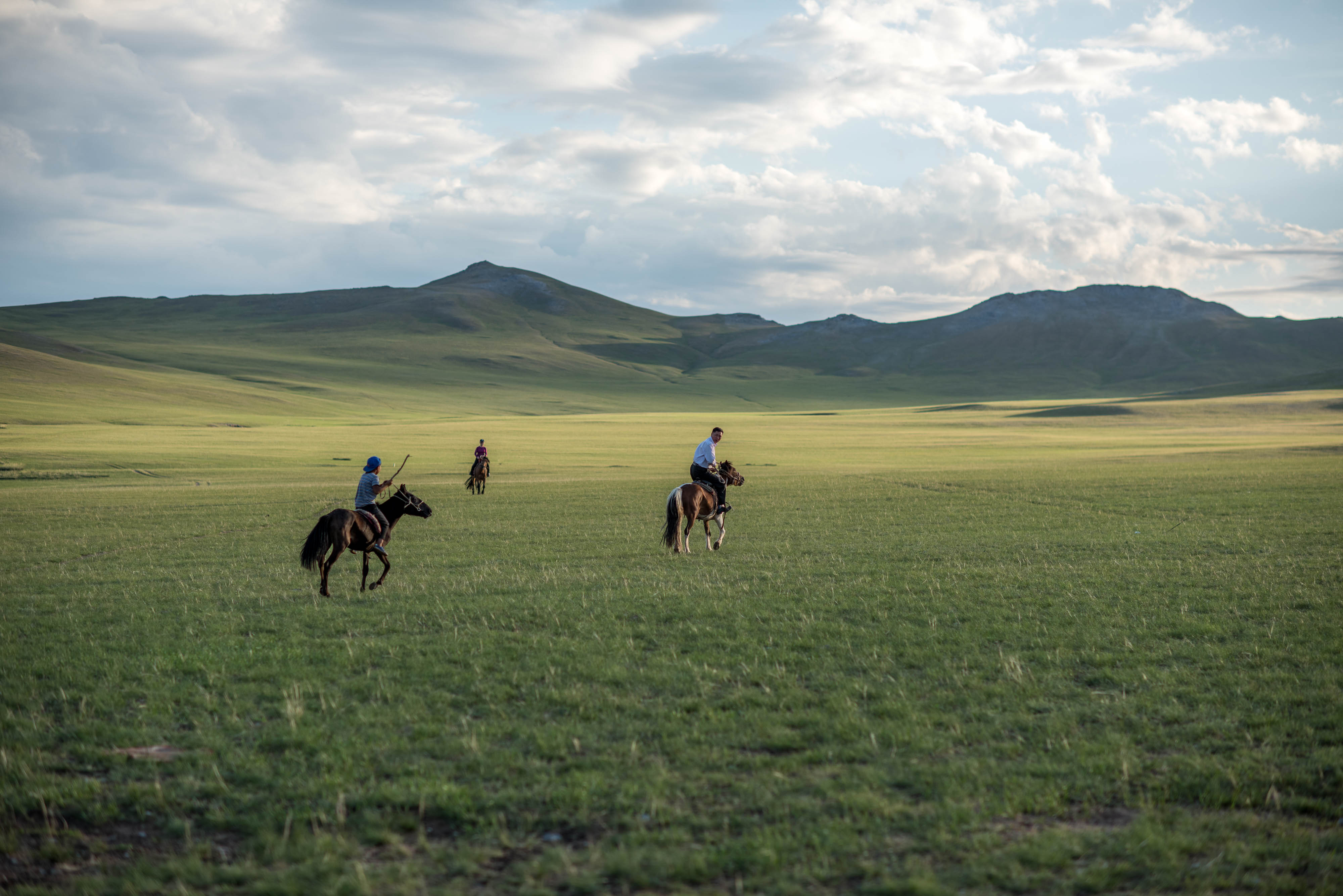 Three people ride horses across a huge expanse of plains.