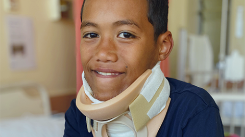 A young boy in a neck brace smiles at the camera.