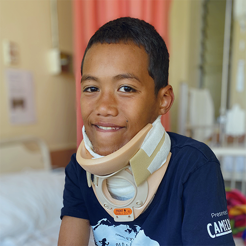 A young boy in a neck brace smiles at the camera.