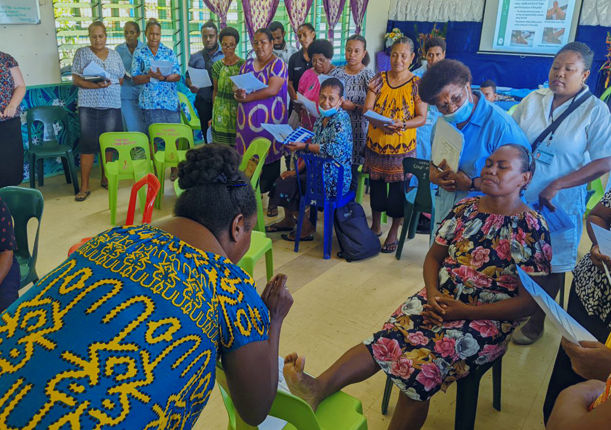 A group of people watch a demonstration of diabetic foot care treatment.