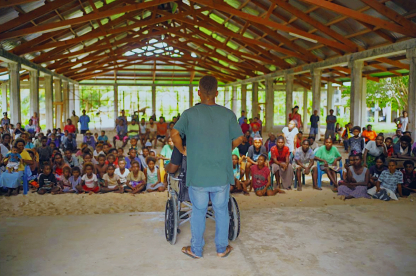 Two people, one standing and one using a wheelchair, perform for a crowd of people.