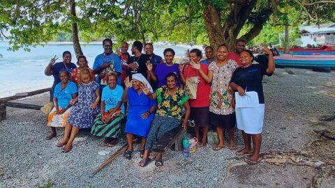 A group of people stand on the beach and smile.