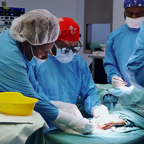 Two people in surgical scrubs delicately perform surgery on the hand of an unseen patient.