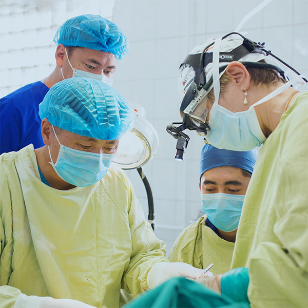 A group of four people in surgical scrubs operate on an unseen patient.