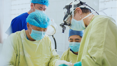 A group of four people in surgical scrubs perform an operation on an unseen patient.