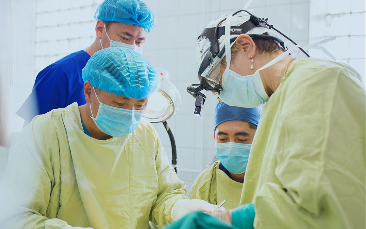 A group of four people in surgical scrubs perform an operation on an unseen patient.