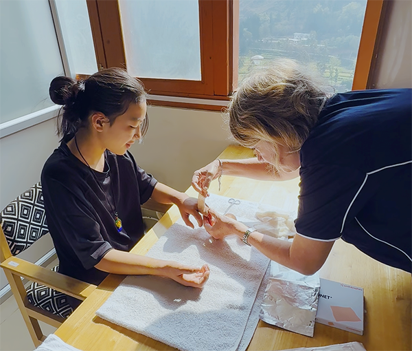 A young girl has her hand carefully dressed in a bandage by a woman.